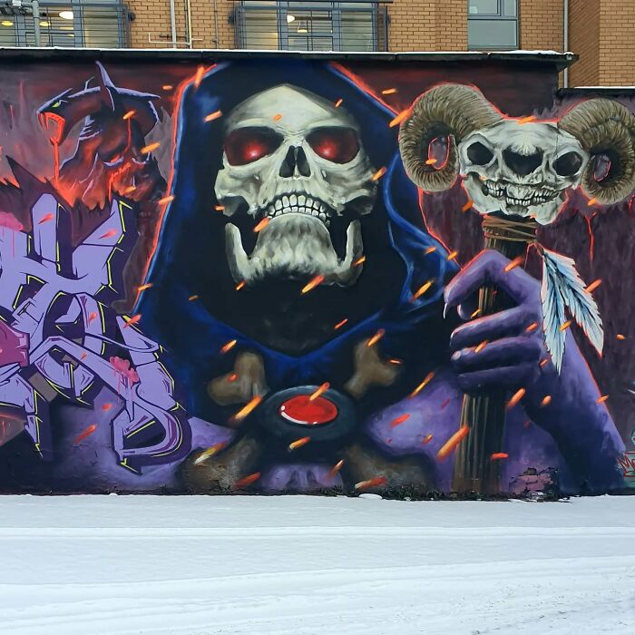 A stunning mural in Glasgow featuring a skeletal figure in a cloak with a staff adorned with skulls and feathers.