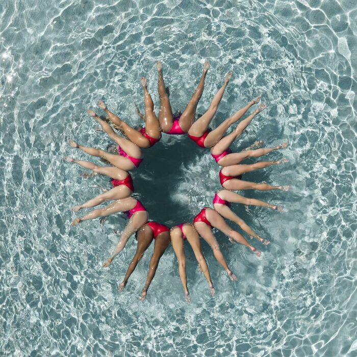 Aerial conceptual photography of synchronized swimmers forming a circle in water, captured by Brad Walls.