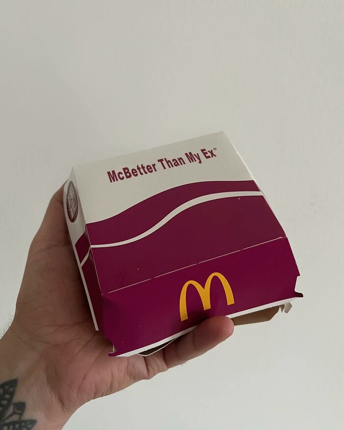 Hand holding a transformed fast food box, altered into a thought-provoking artwork with text "McBetter Than My Ex".