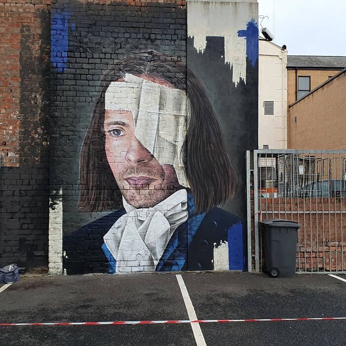 Glasgow mural depicting a man with long hair and a bandaged eye, painted on a brick wall.
