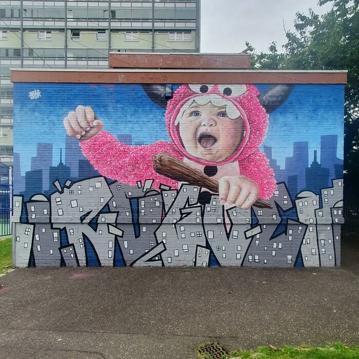 Mural of a child in a pink costume on a Glasgow wall, with graffiti-style text and cityscape background.
