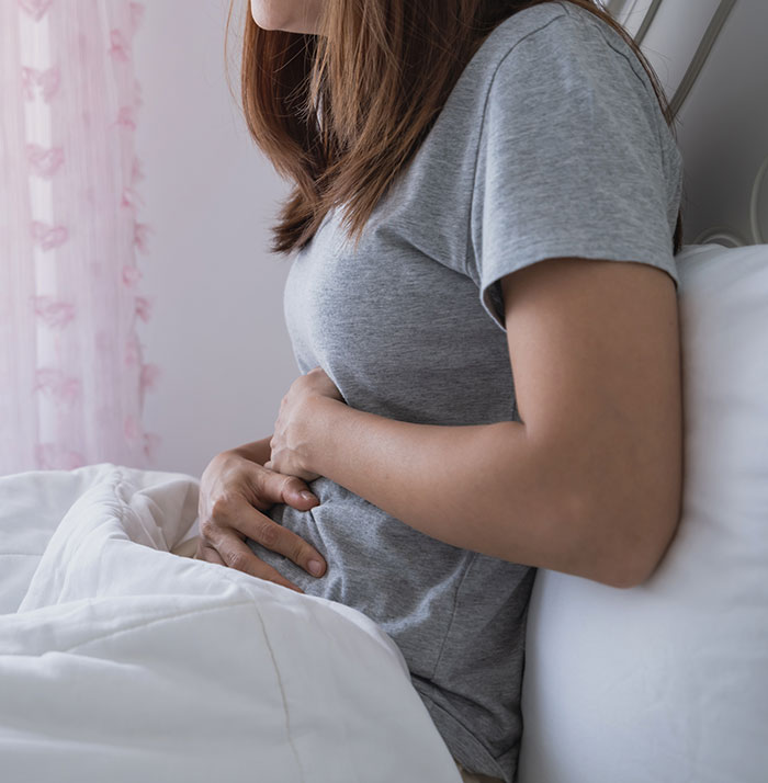 Woman in grey shirt clutching her abdomen in apparent discomfort, possibly due to an incorrect medical diagnosis.