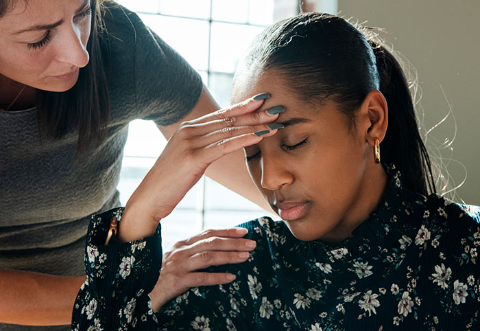 A concerned woman comforts another with a headache, possibly pondering an incorrect medical diagnosis.