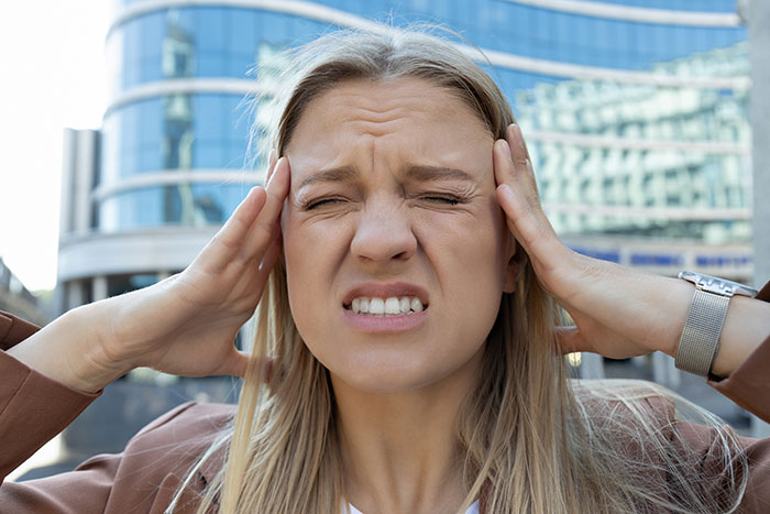 A woman outdoors holding her head, expressing discomfort; related to unhinged medical diagnosis.