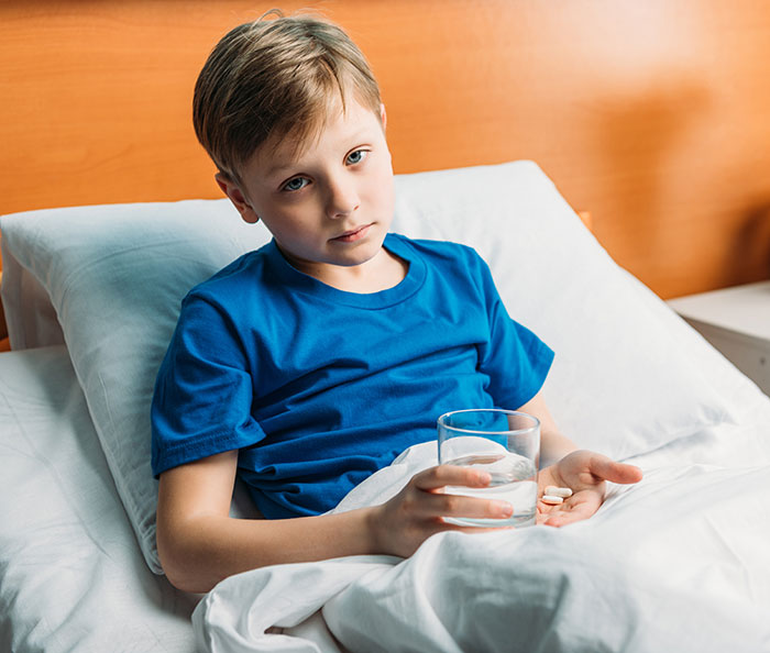 Young boy in bed holding pills and a glass of water, illustrating an incorrect medical diagnosis experience.