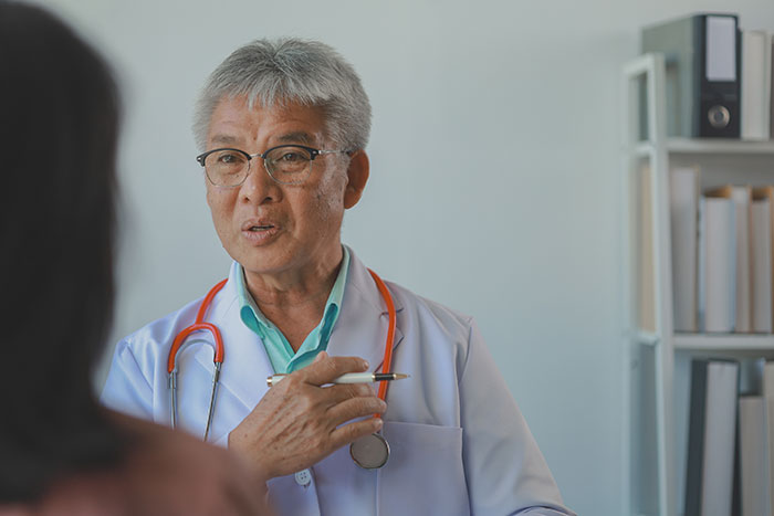 Doctor discussing a medical diagnosis with a patient, holding a pen and wearing a stethoscope.