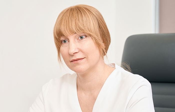 A woman in a white top, sitting in a chair, looking thoughtful, related to unhinged medical diagnosis discussions.