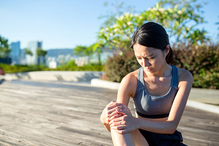 A woman outdoors holds her knee in pain, reflecting on an incorrect medical diagnosis experience.