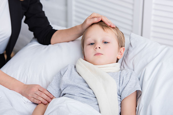 Young boy in bed with an incorrect medical diagnosis, comforted by an adult's hand on his forehead.