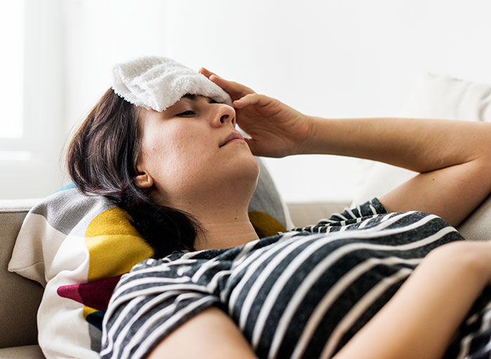Woman lying on a couch, holding a cold compress to her forehead, possibly dealing with an incorrect medical diagnosis.