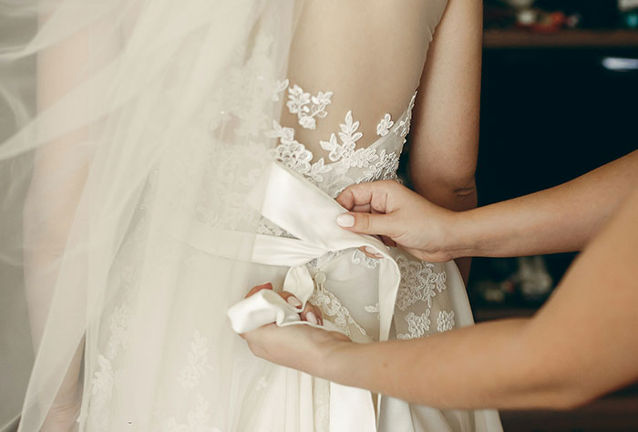 Bride in lace gown, hands adjusting bow, representing wedding tensions.