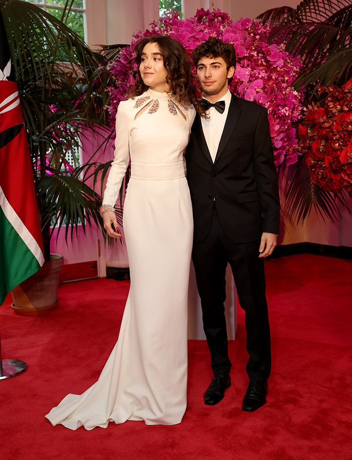 Young couple in formal attire at a glamorous event, posing by vibrant floral arrangements.