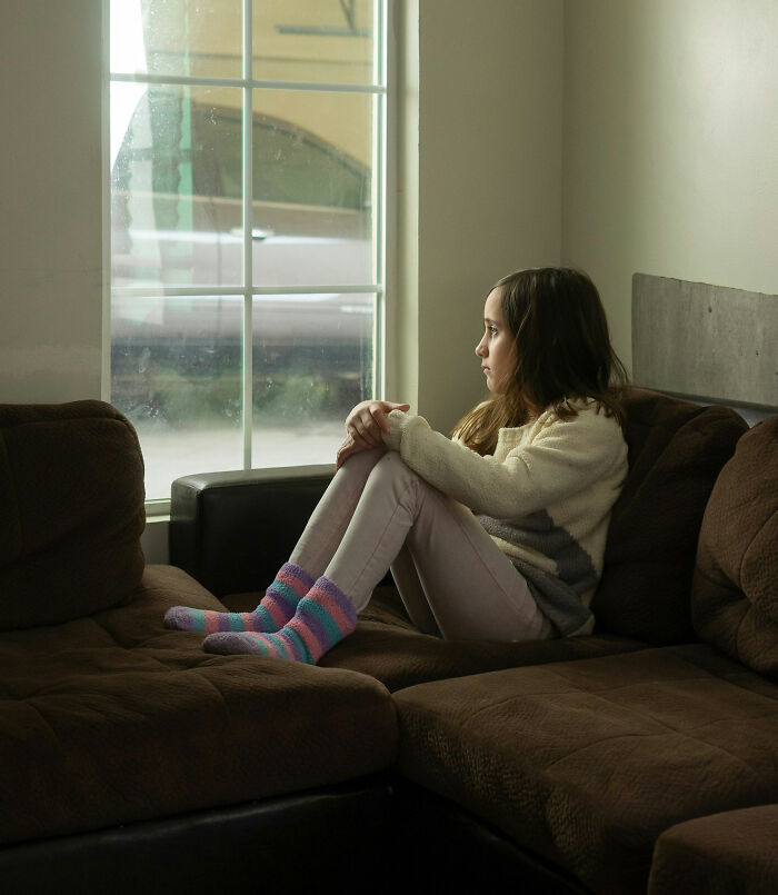 Child sitting alone on a couch, gazing out a window, capturing a moment of deep reflection and potential trauma.