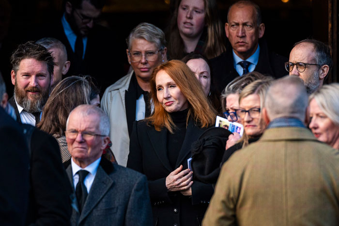 A woman with red hair stands among a group of people, wearing a black coat, after a Supreme Court ruling on trans rights.