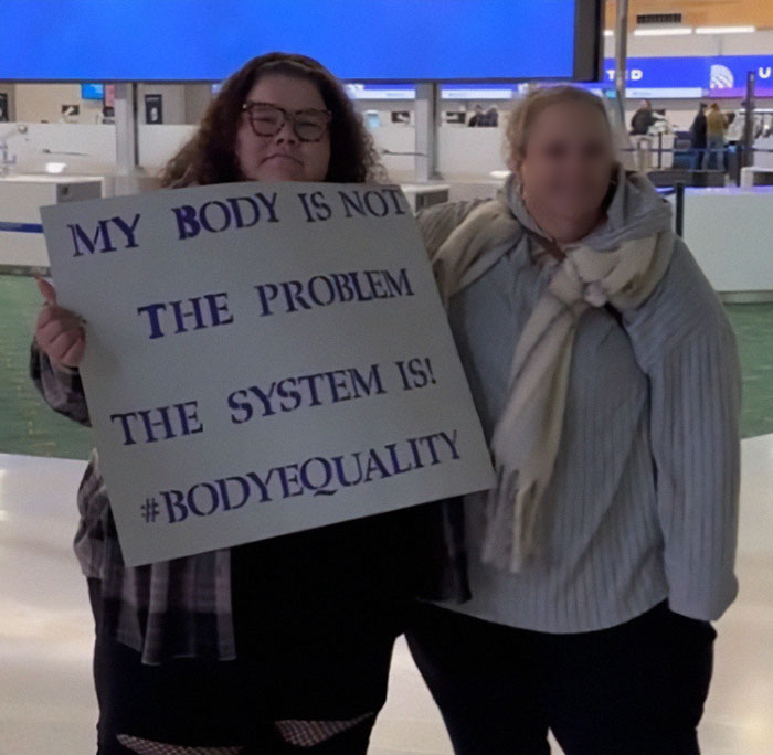 Plus-sized passenger holding sign about body equality at airport.
