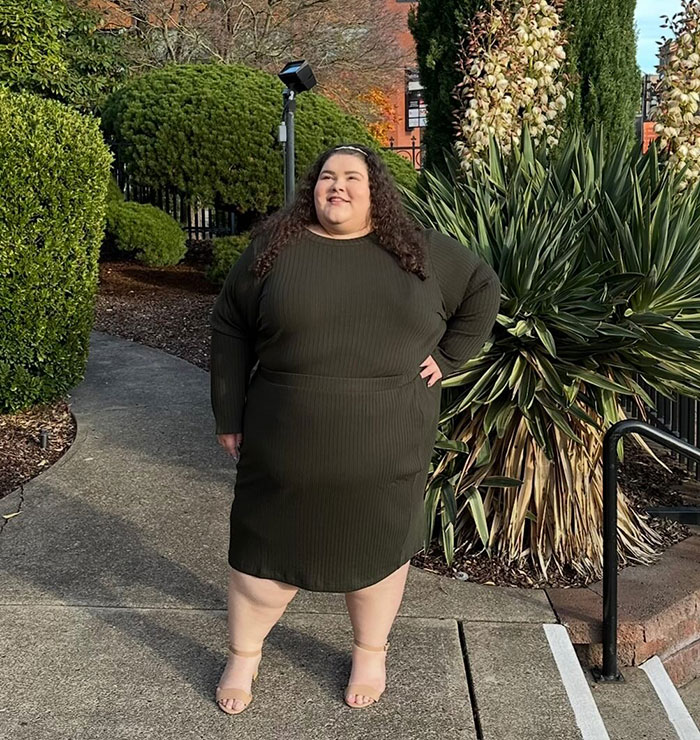 Plus-sized passenger standing outdoors in a green dress, surrounded by greenery.