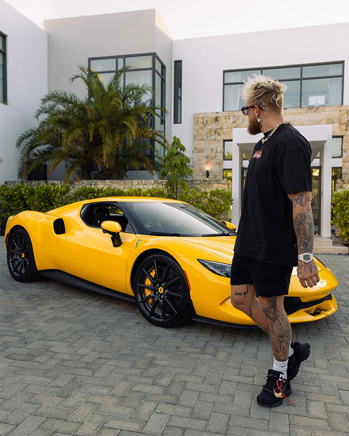 Jake Paul with tattoos standing near a yellow sports car outside a modern house, highlighting YouTube fame success.