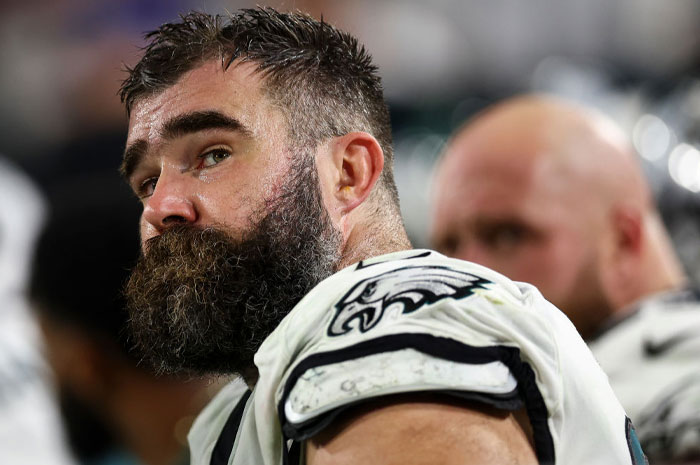 Former Eagle Jason Kelce on the sidelines, wearing a football uniform, highlighting his sports career and fortune.