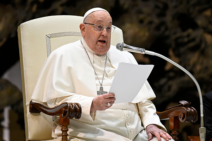 Pope Francis speaking into a microphone while holding a paper during a formal address.