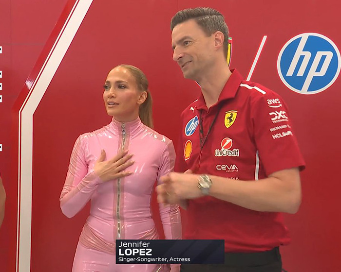 Jennifer Lopez in a pink catsuit at Saudi F1 race, standing with a man in a red Ferrari shirt.