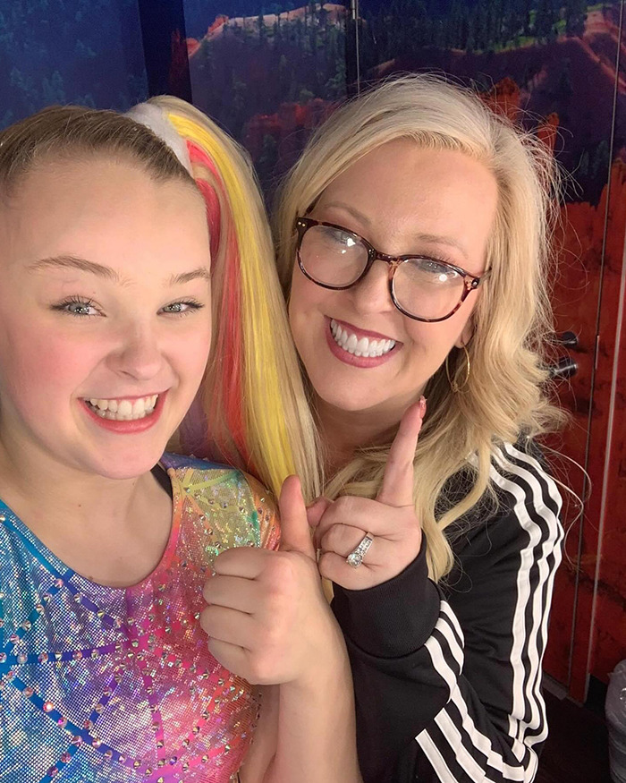JoJo Siwa smiling with a woman in colorful dance attire, amid Dance Moms controversy discussions. JoJo Siwa smiling with a woman in colorful dance attire, amid Dance Moms controversy discussions.