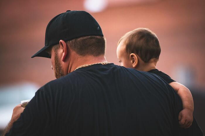 Man wearing black cap holding baby, symbolizing connection as ladies share red pill stories in a heartfelt moment.