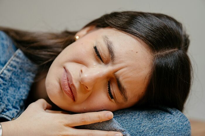 Young woman with tears lying on denim-clad knee, showing emotion related to relationship arguments and struggles.