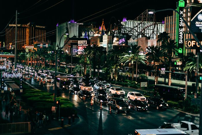 Nighttime view of a busy street in Las Vegas with bright lights and palm trees, capturing a tourist experience.