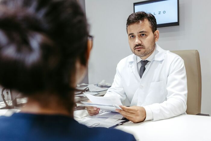 Male doctor in white coat discussing medical documents with female patient, highlighting unfair treatment from doctors.