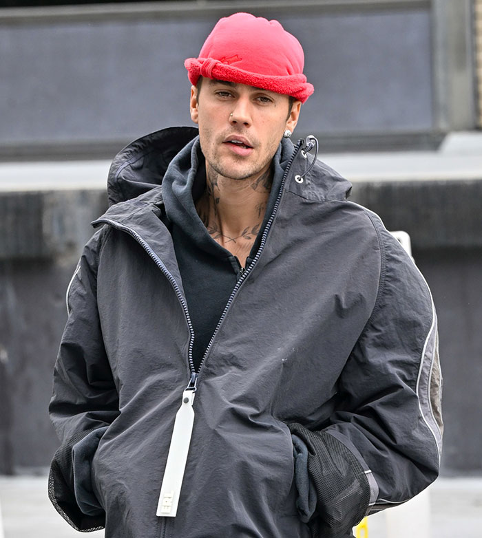 Young man in a red hat and black jacket outside, hands in pockets.