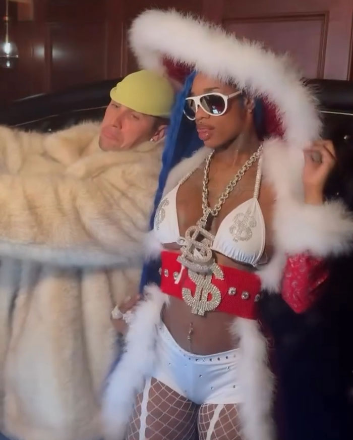 Justin Bieber dressed in a furry coat, standing beside a female rapper in a bold outfit, capturing attention.