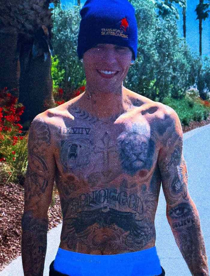 Justin Bieber outdoors, smiling in a beanie and showcasing tattoos, surrounded by greenery.