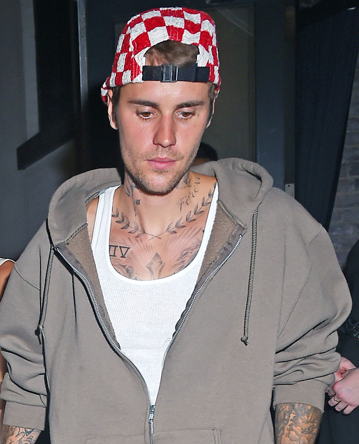 Justin Bieber in a casual outfit, wearing a red checkered hat, walking outside at night.