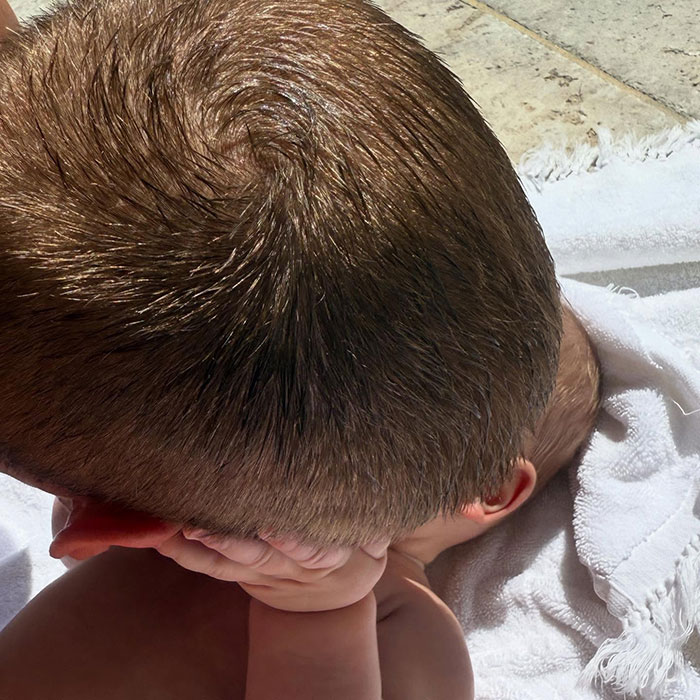 Baby by the poolside wrapped in a towel, with short hair exposed to sunlight, sparking internet debate.