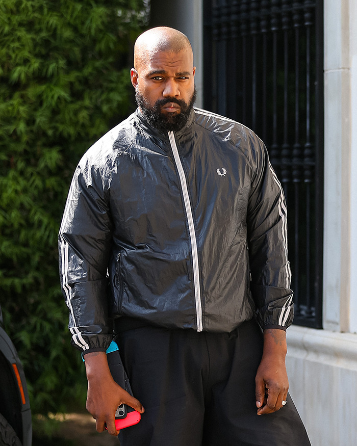 Man in black tracksuit holding phone outdoors, looking serious.