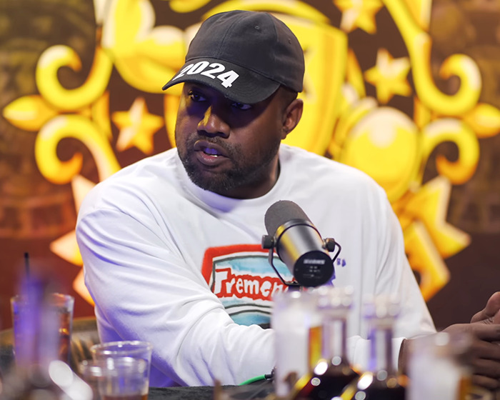 A man in a 2024 hat speaks into a microphone during an interview, with a colorful background.