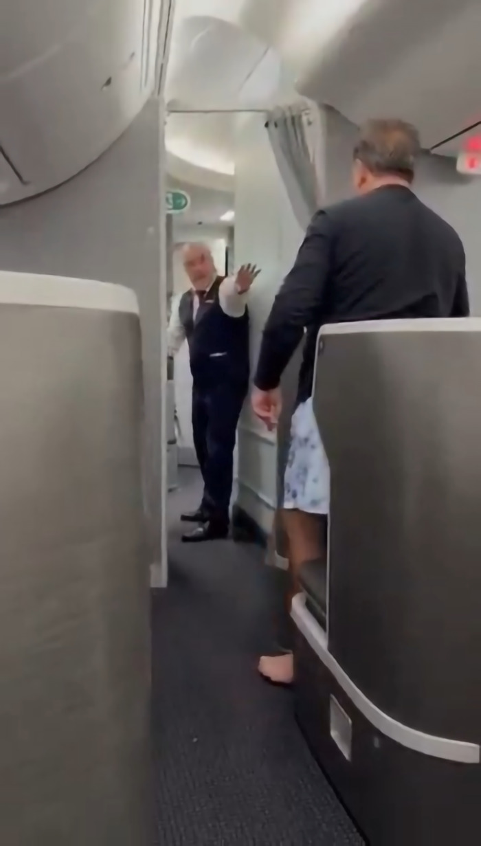 Flight crew blocking a passenger trying to storm cockpit during a delay inside an airplane cabin.