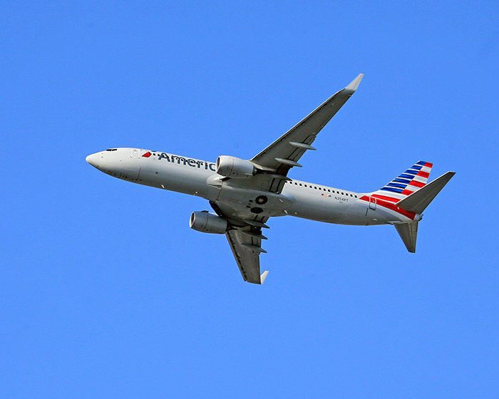 Commercial airplane in flight against clear blue sky representing flight delay incident with passenger confrontation.