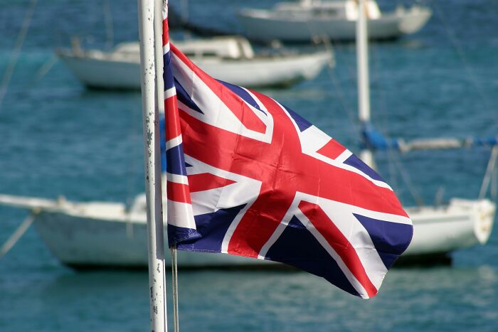 Union Jack flag waving with blurred boats on a blue water background.