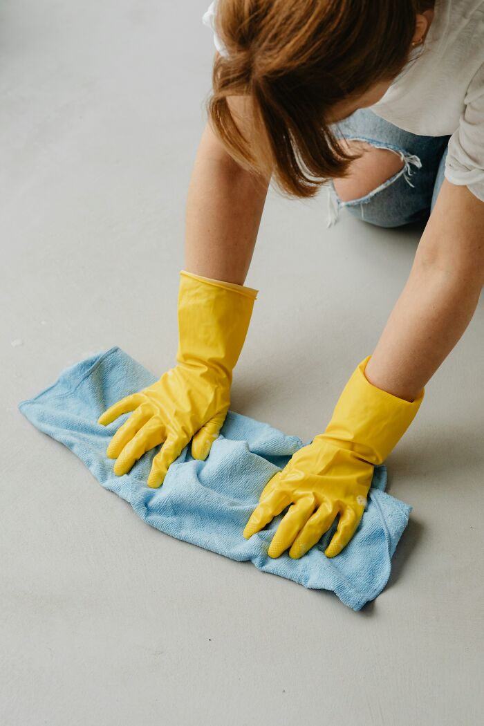 Person wearing yellow gloves, cleaning a floor with a blue cloth, illustrating strict cleaning rules.