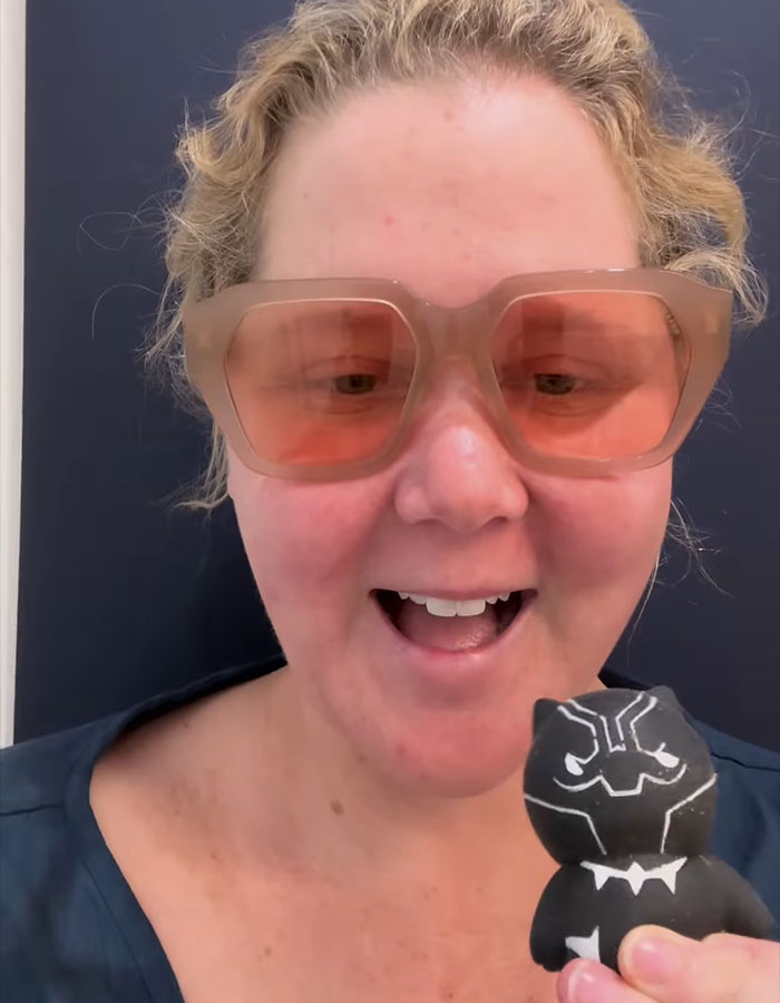 Woman with oversized sunglasses holding a small Black Panther figure, smiling in a casual setting. Woman with oversized sunglasses holding a small Black Panther figure, smiling in a casual setting.