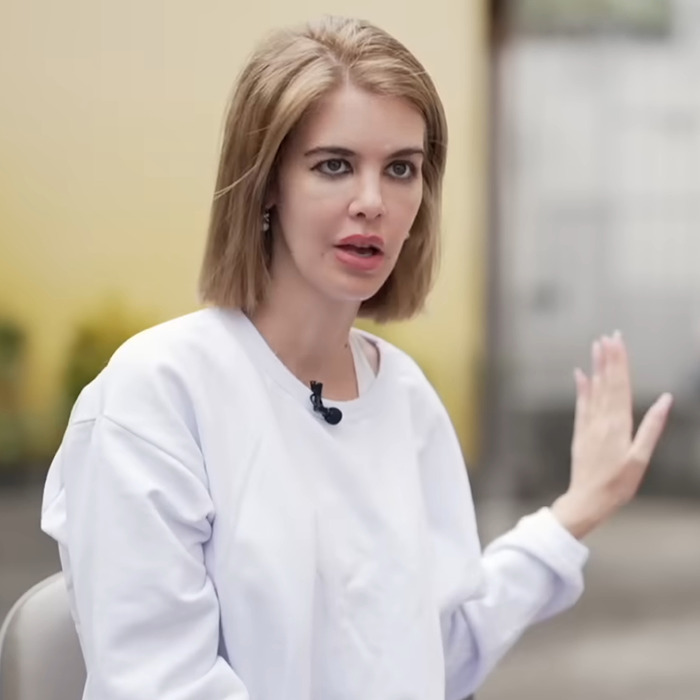 A woman in a white sweatshirt gestures during an interview about the influencer's alleged scam.