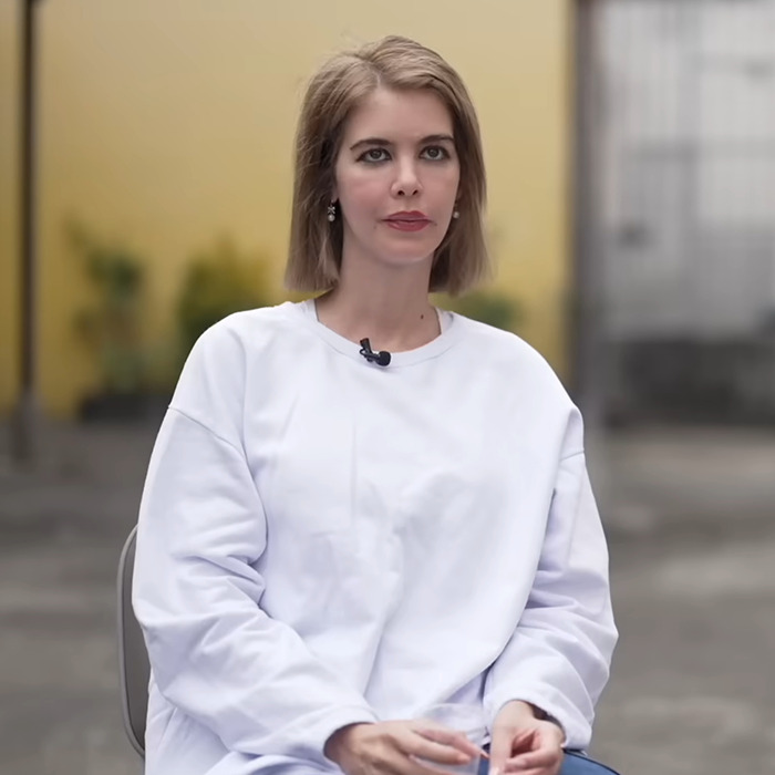 Woman in a white shirt sitting outdoors with a microphone, related to Leonardo DiCaprio's influencer ex documentary.