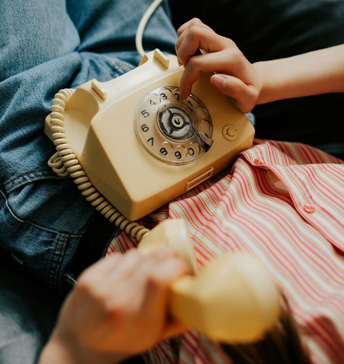Person using a vintage rotary phone, wearing a striped shirt and jeans, illustrating loophole exploitation.