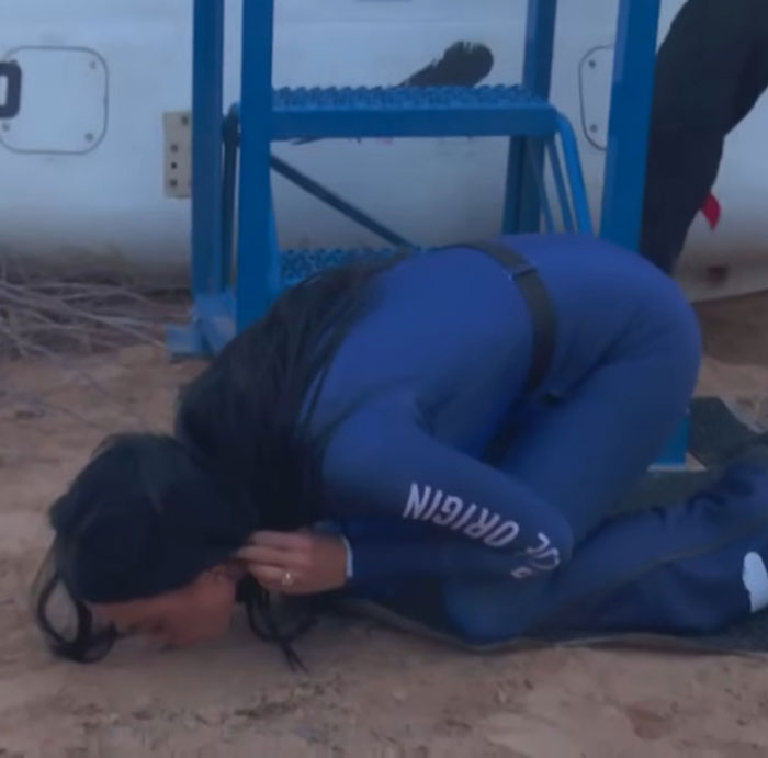 Person in a blue "Origin" suit humorously crouching by a ladder, satirizing Katy Perry's Blue Origin flight. Person in a blue "Origin" suit humorously crouching by a ladder, satirizing Katy Perry's Blue Origin flight.