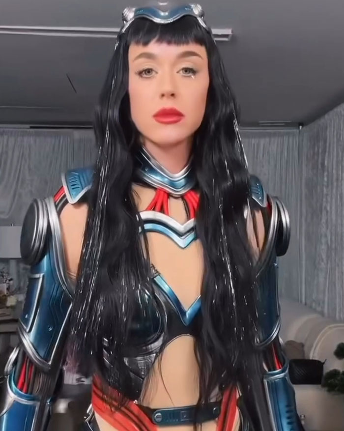 Katy Perry in futuristic armor costume with long black hair, addressing critics of her Blue Origin space flight.