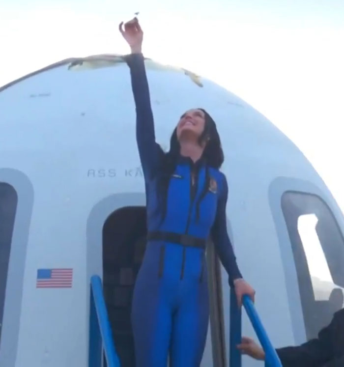 Woman in blue astronaut suit reaching upwards outside a capsule, symbolizing support for Katy Perry.