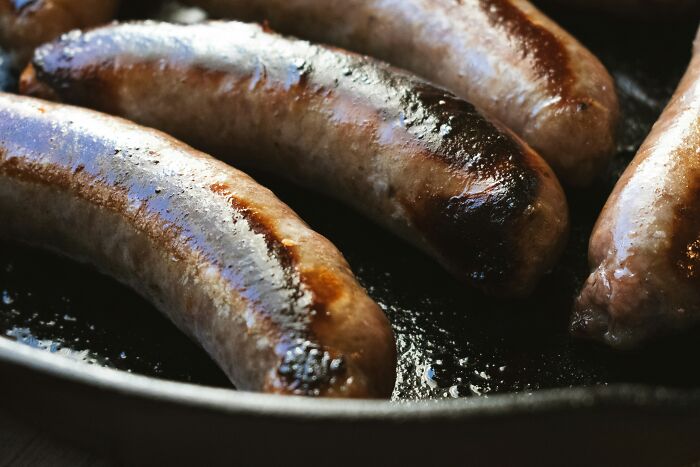 Cheddar bratwursts in a skillet, involved in a recall due to hard plastic found in products.
