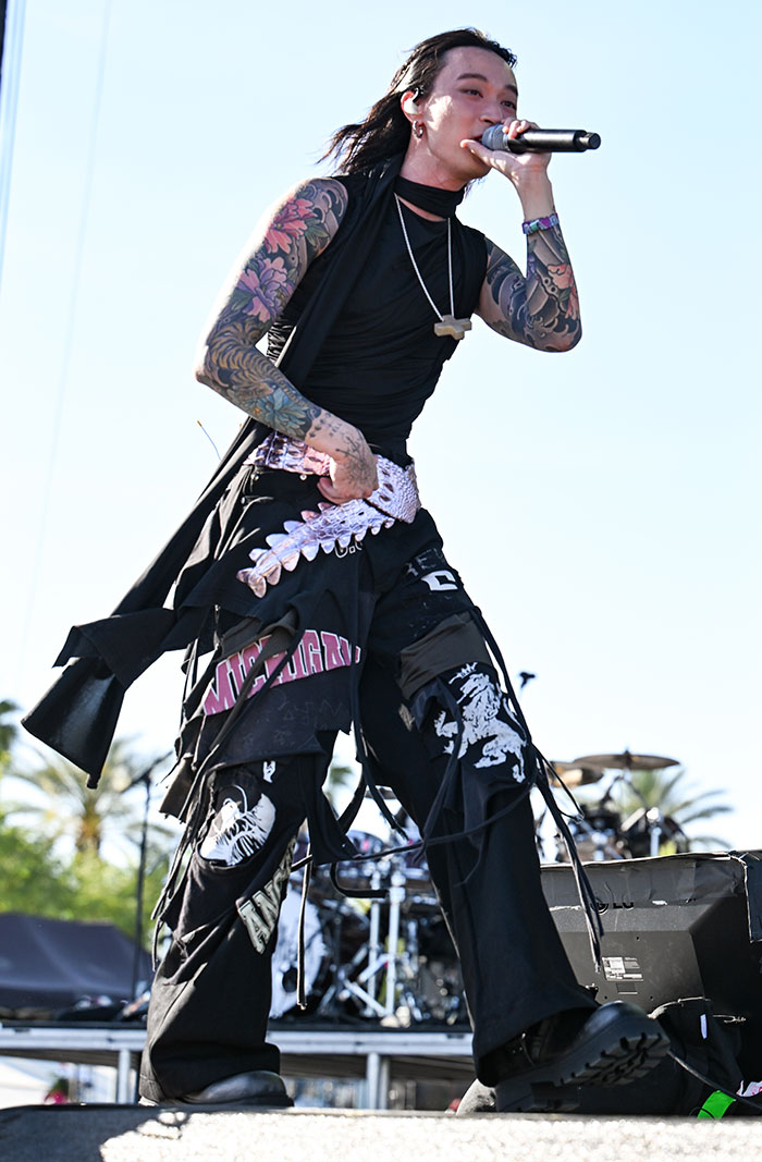 Celebrity on stage at Coachella 2025, wearing eclectic fashion with tattoos visible, performing with a microphone.