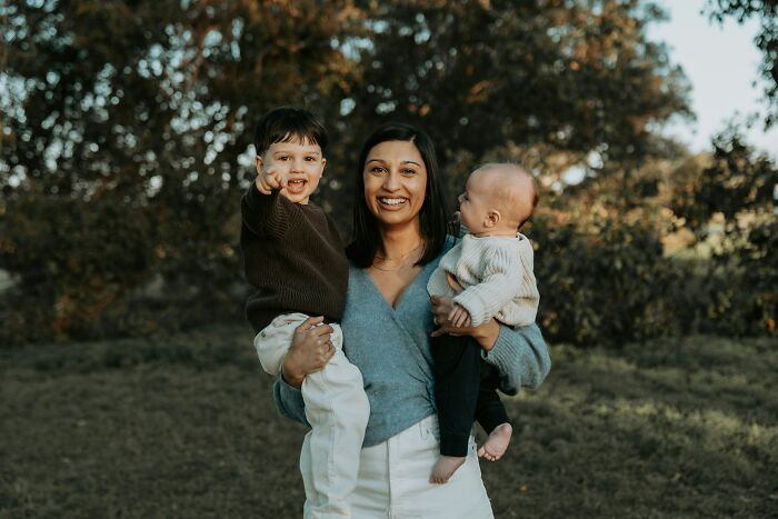 Woman outdoors holding two children smiling and sharing red pill stories in a natural setting with trees in background